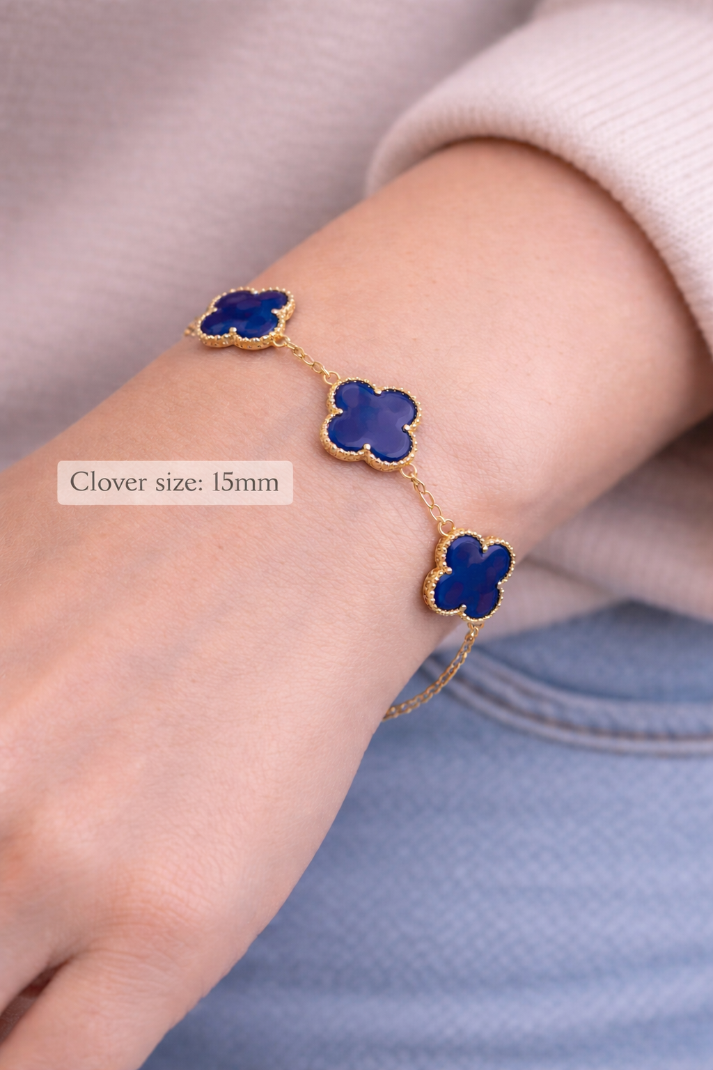 Gold bracelet with blue clover-shaped charms on a wrist.
