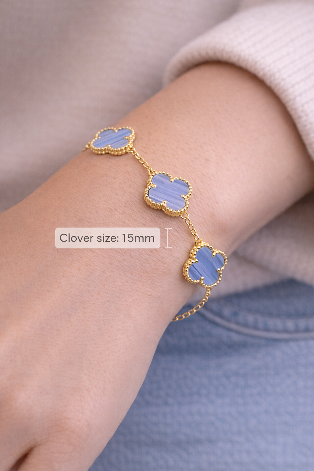 Gold bracelet with blue clover-shaped charms on a wrist against a neutral background