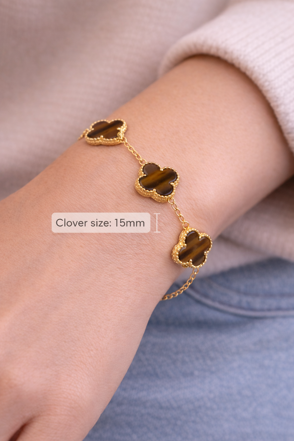 Gold bracelet with clover-shaped charms on a wrist against a neutral background