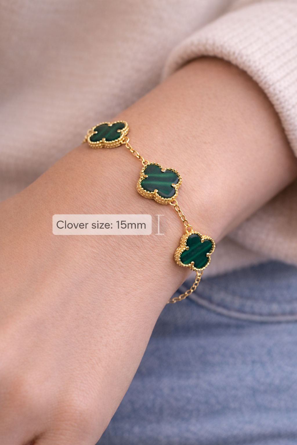 Gold bracelet with green clover-shaped charms on a wrist against a neutral background