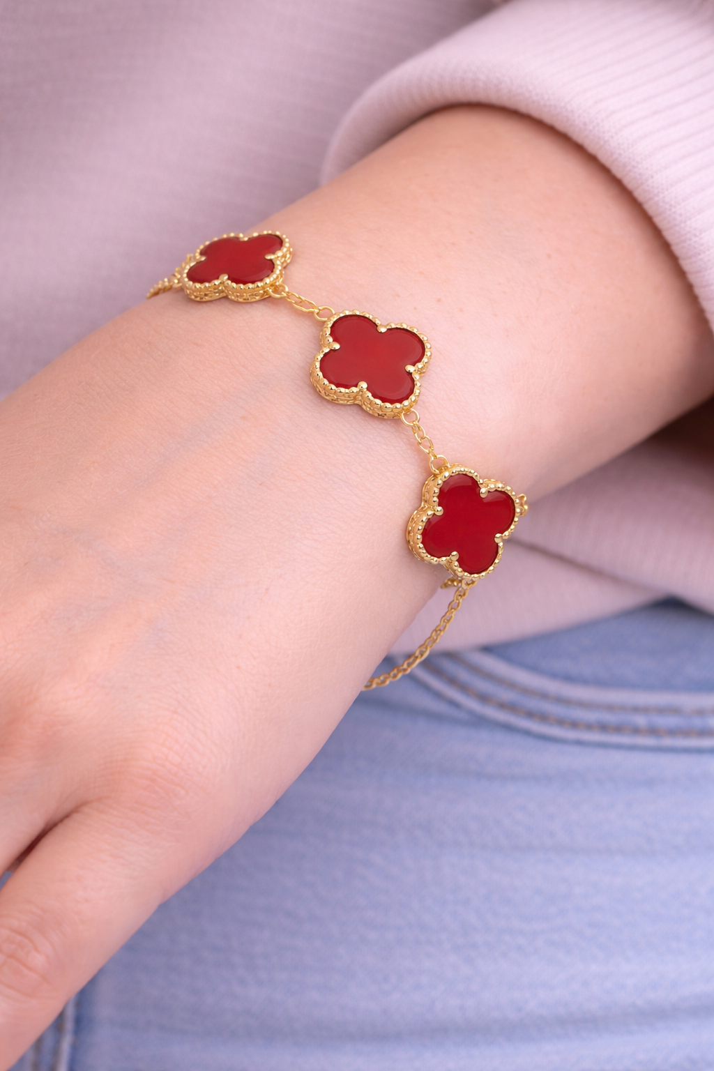 Bracelet with red clover-shaped charms on a wrist against a light background