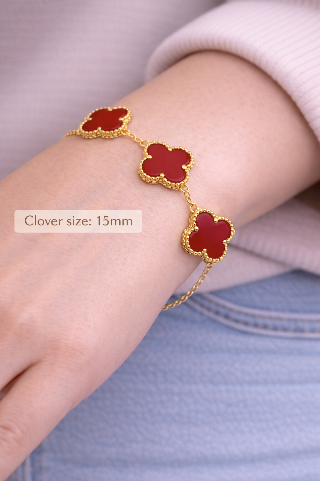 Bracelet with red clover-shaped charms on a wrist, against a light background.
