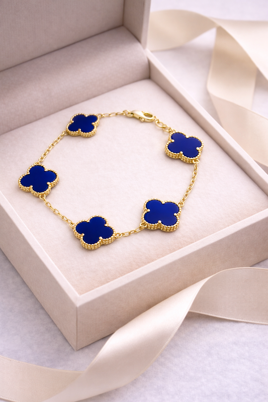 Gold necklace with blue clover-shaped pendants in a beige jewelry box.