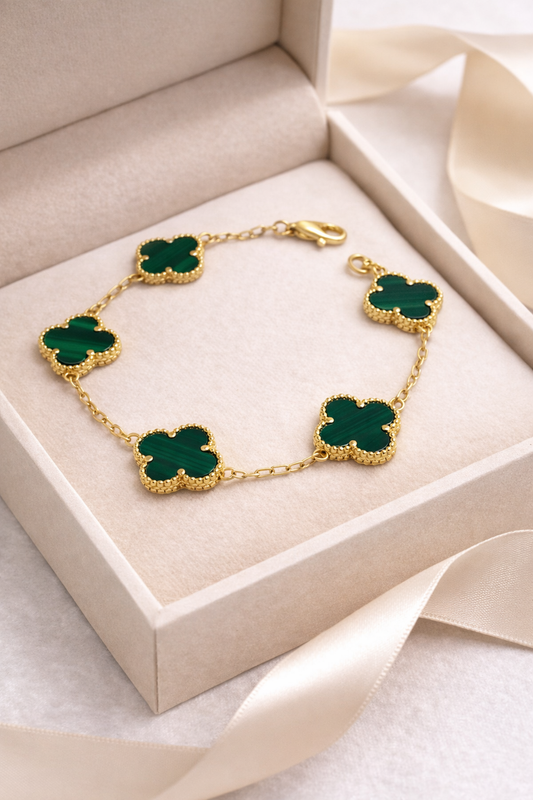 Gold bracelet with green clover-shaped charms in a beige jewelry box.