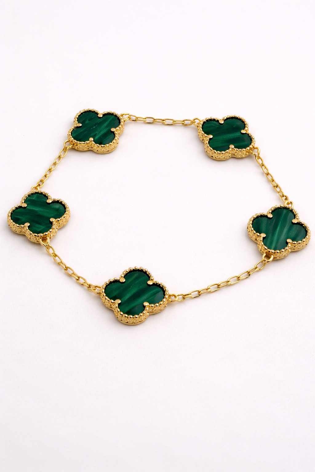 Gold necklace with green clover-shaped stones on a white background