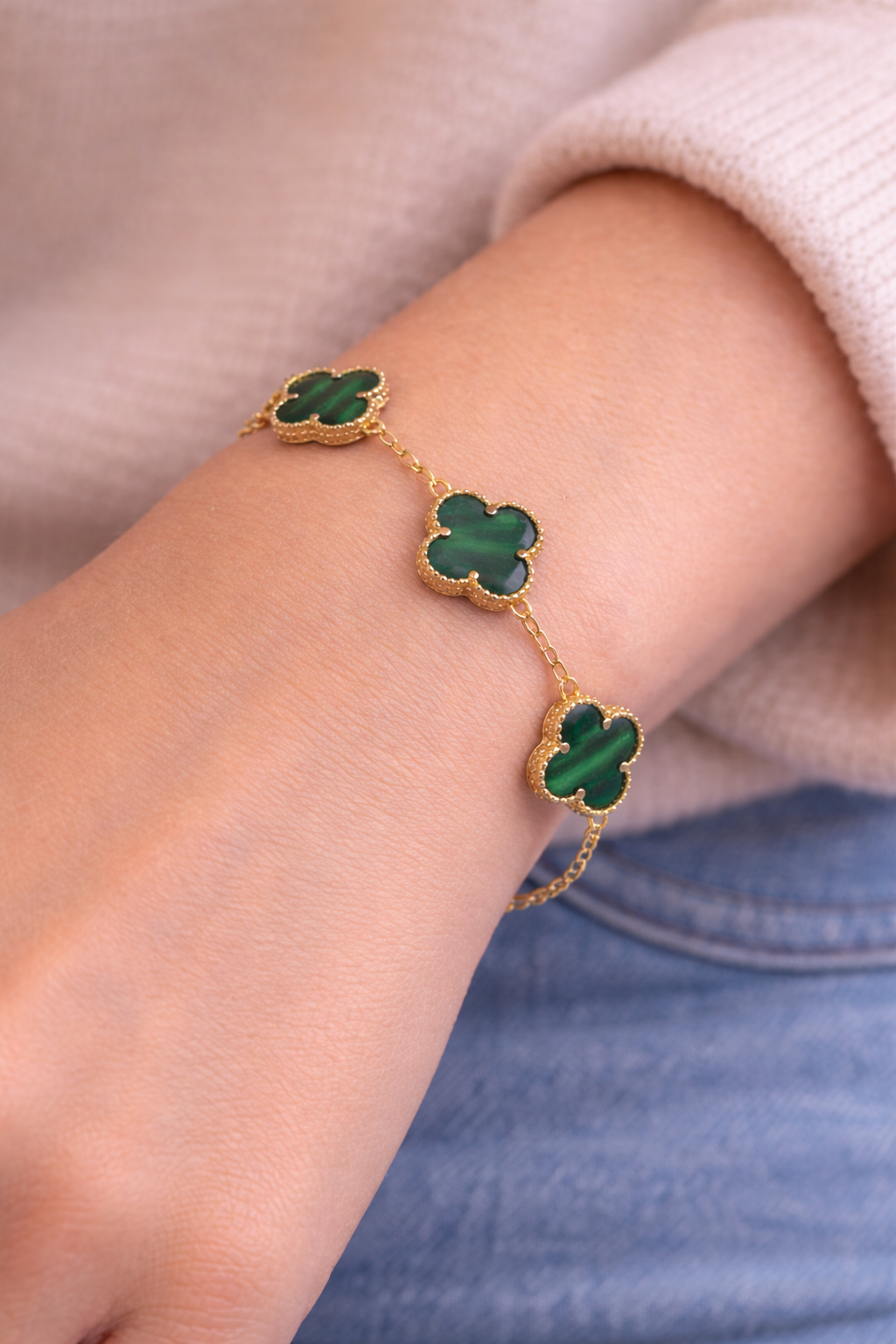 Gold bracelet with green clover-shaped stones on a wrist.
