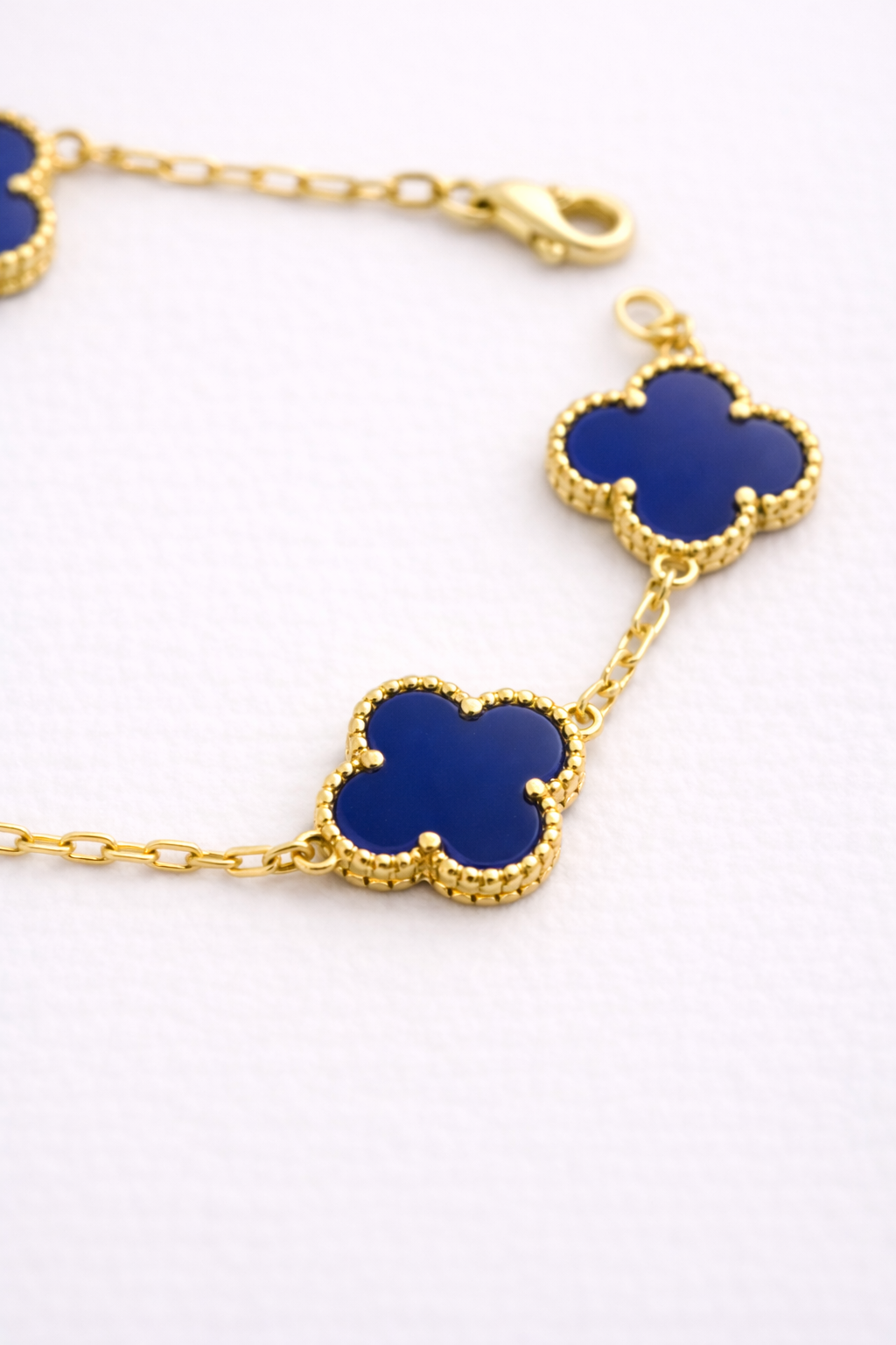 Gold bracelet with blue clover-shaped charms on a white background