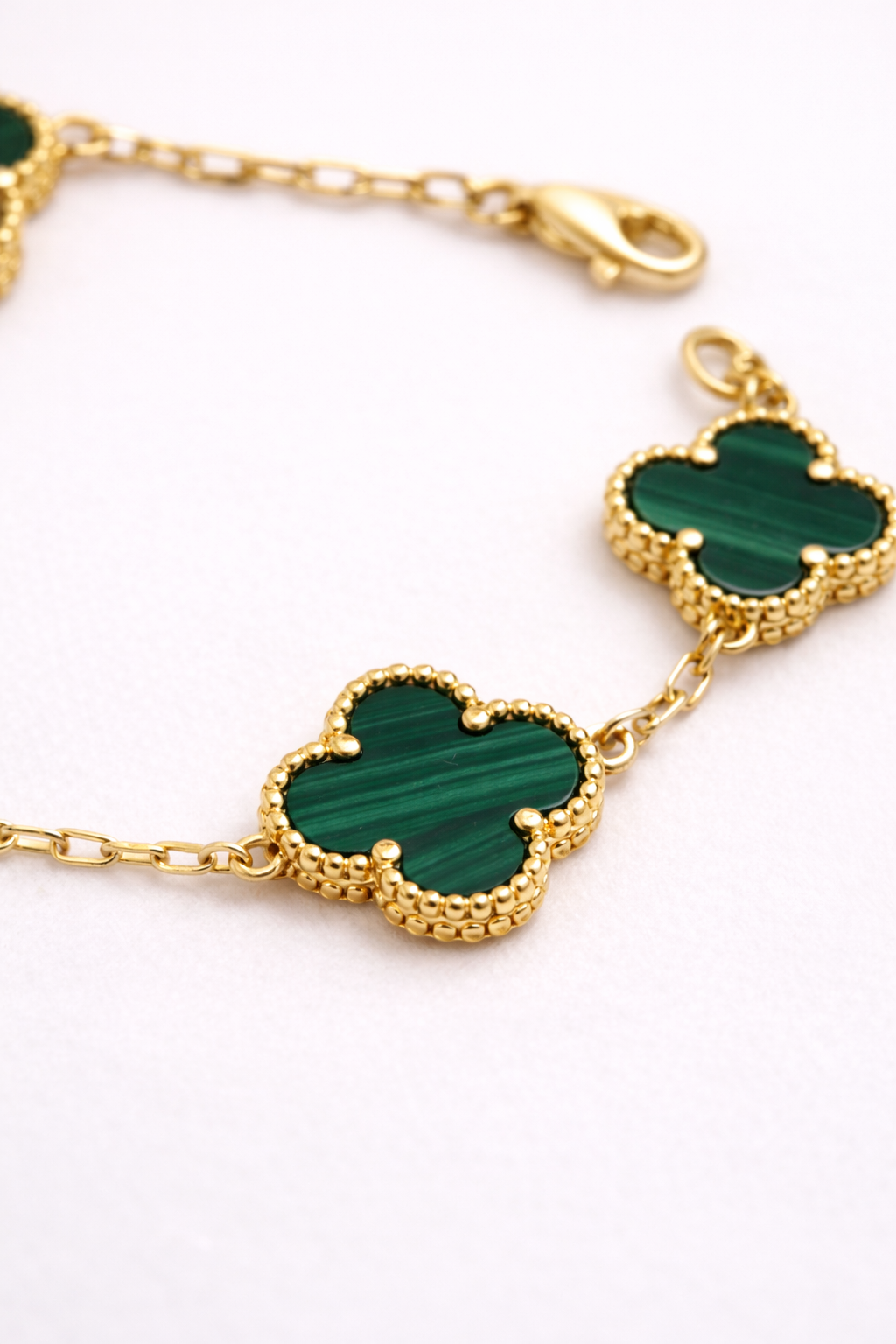 Gold bracelet with green clover-shaped charms on a white background
