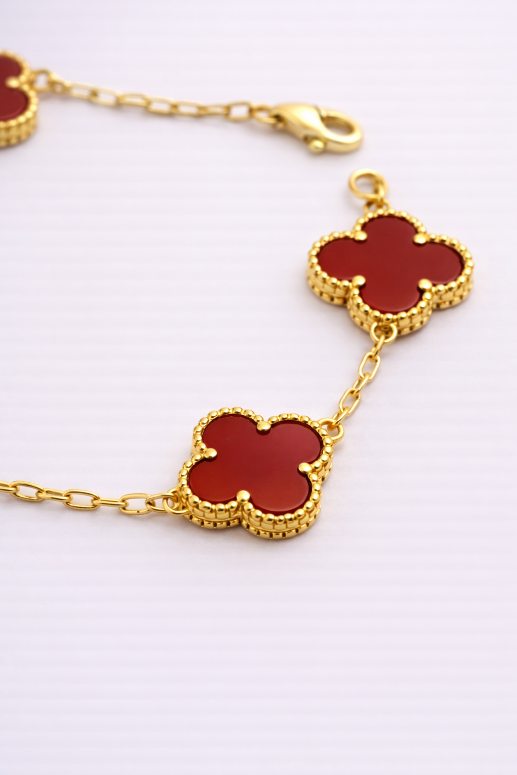 Gold bracelet with red clover-shaped charms on a white background