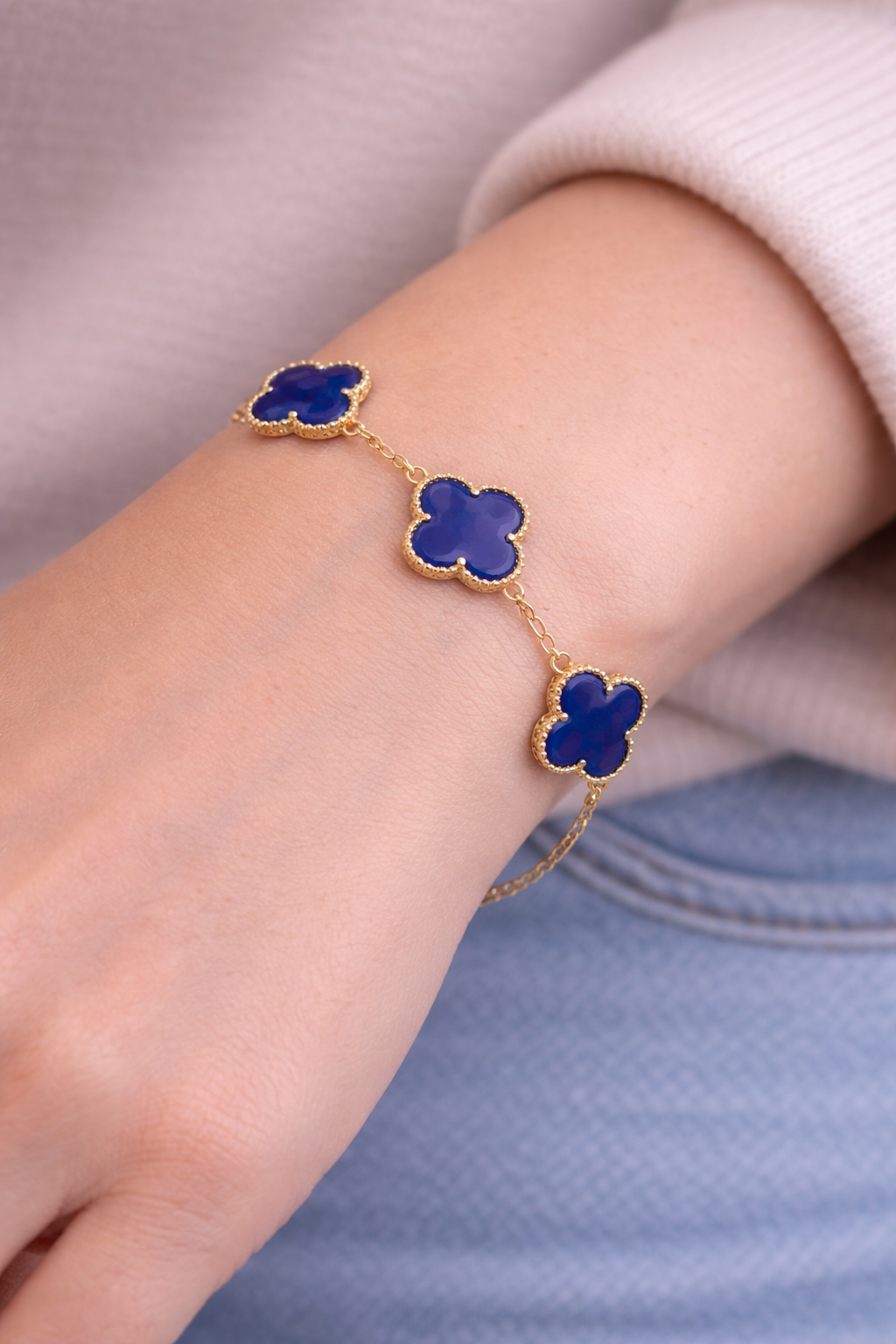 Bracelet with blue clover-shaped charms on a wrist against a neutral background