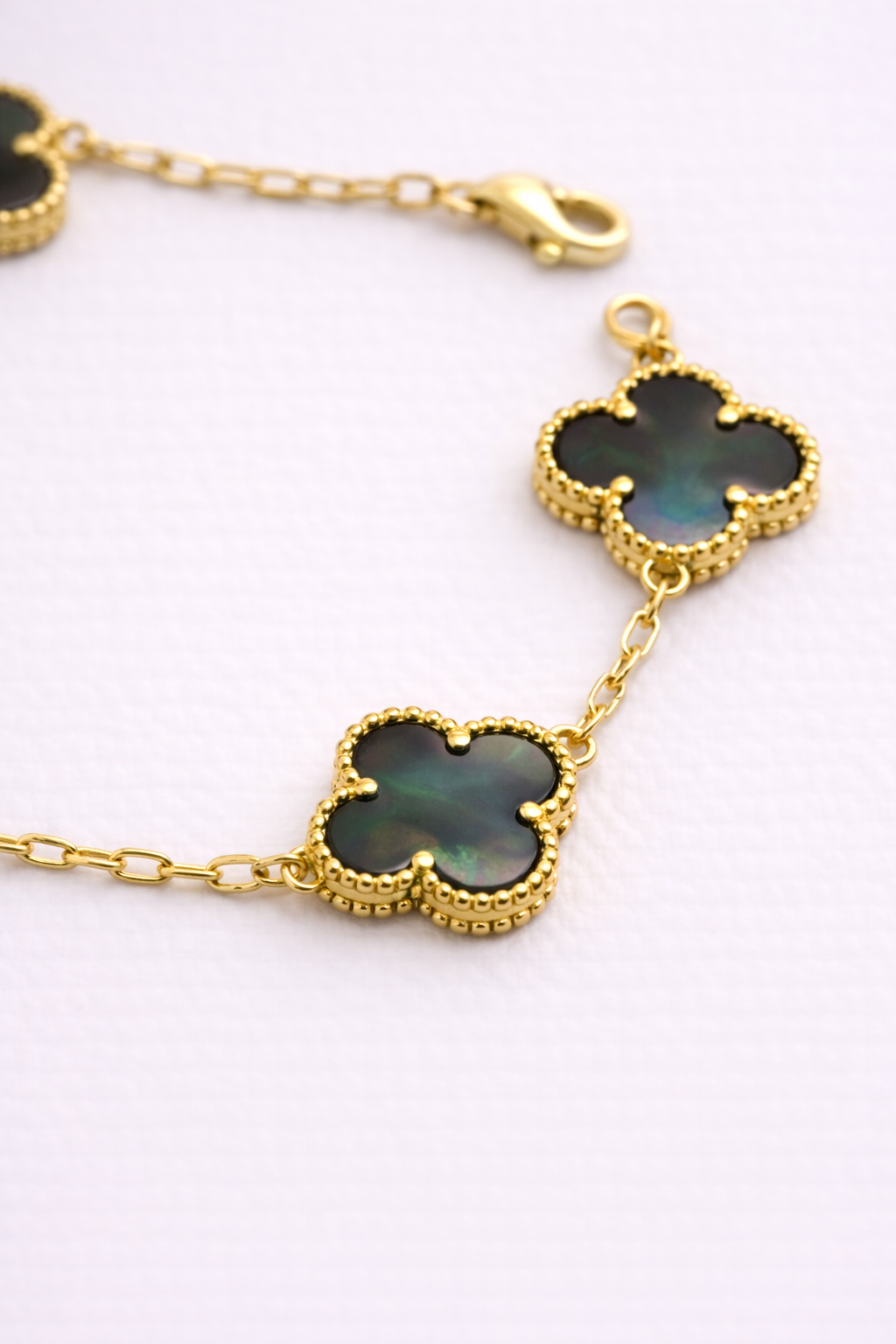 Close-up of gray mother of pearl clover bracelet with textured gold bezel