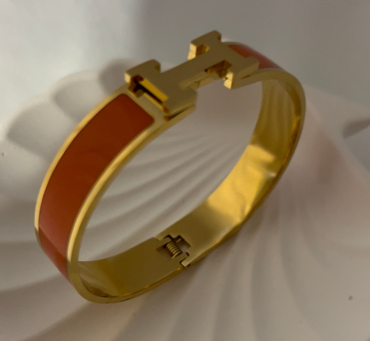 Side angle of orange H bangle bracelet with glossy enamel and gold finish, modern elegant bracelet