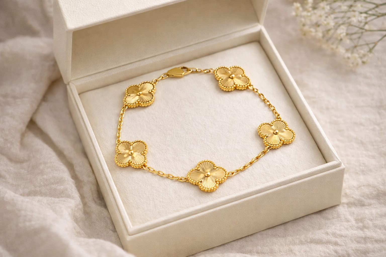 Gold bracelet with floral designs in a white box on a soft fabric background